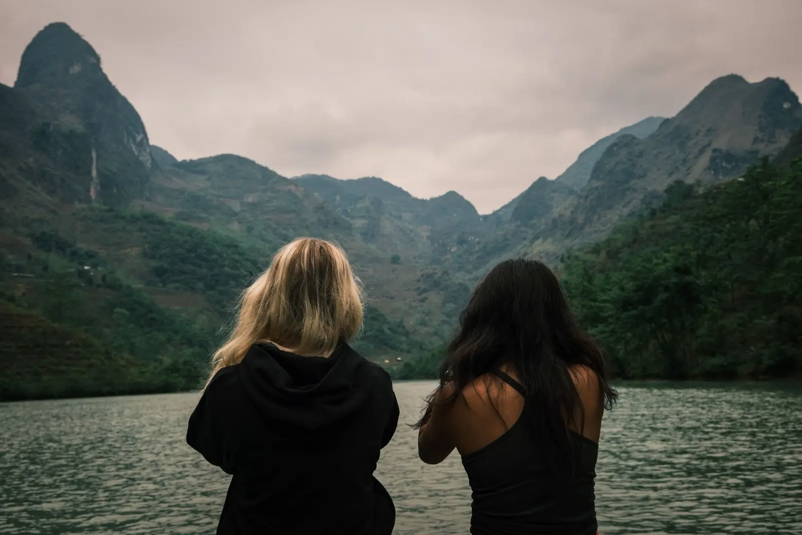Two travellers sitting side by side, looking out over a river towards misty mountains